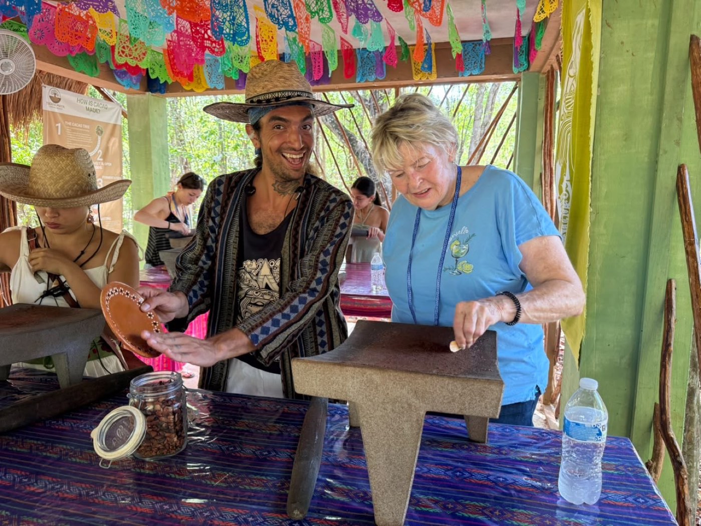 A guide laughing with a guest grinding cacao on a stone metate